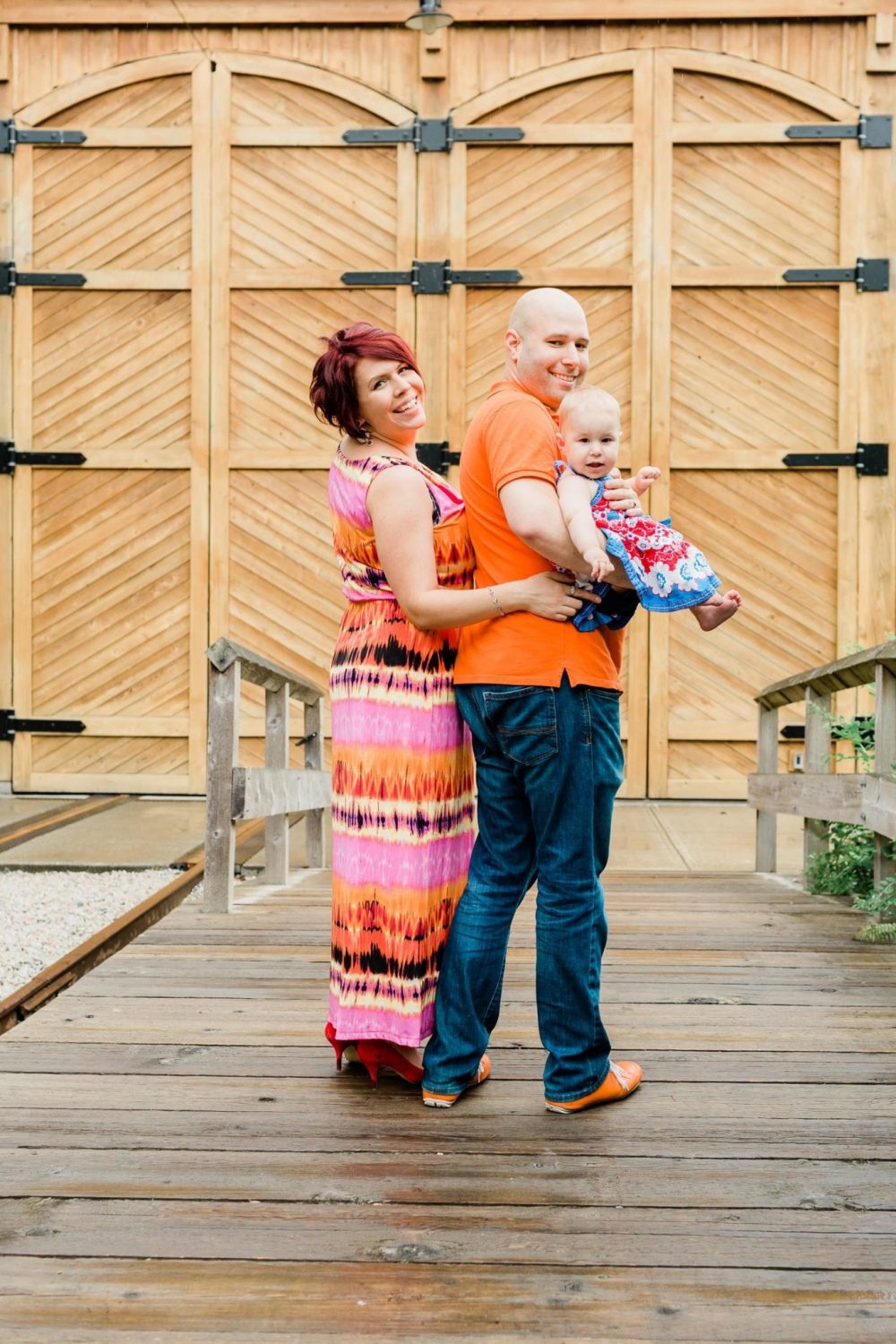 Couple standing holding a baby and looking back smiling. Family Photo in Burnaby Village Museum